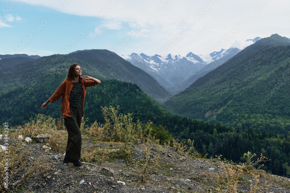 Fototapeta premium A hiker stands on a rocky outcrop overlooking a vast mountain landscape, soaking in the fresh air and dramatic valley below, conveying adventure and solitude in wild nature