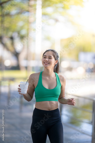 Asian woman jogger drinking smoothie in urban park