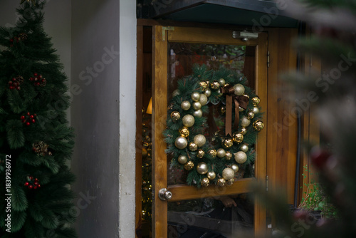Christmas wreath adorned with gold ornaments hangs on a wooden door, adding holiday cheer to the entrance
