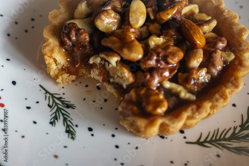 Traditional Christmas tart with nuts and salted caramel on decorated plate. Bitten tart on festive Christmas plate. Bitten hazelnut cake close up. Cinnamon cookie with caramel. Winter holiday food