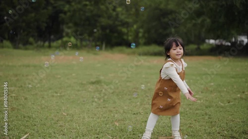 slow motion of happy toddler girl running and playing soap bubble in grass field 