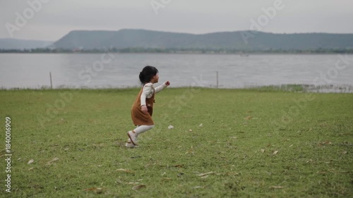 slow motion of toddler girl running on a grass field near the river