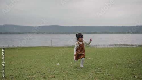slow motion of toddler girl running on a grass field near the river