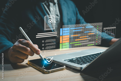 Businessman managing digital project workflow using laptop and smartphone with virtual checklist, timeline, progress tracking interface, representing planning, productivity, modern work management.