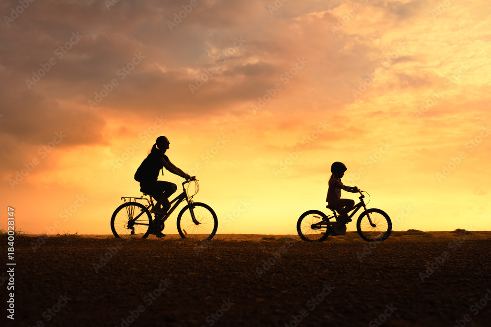 Fototapeta premium Silhouette of Woman and Child Biking in Nature at Sunset – Summer Adventure