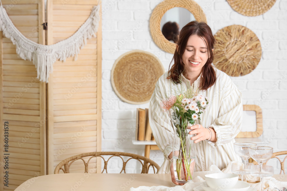 Fototapeta premium Pretty young woman serving table with beautiful flowers in dining room