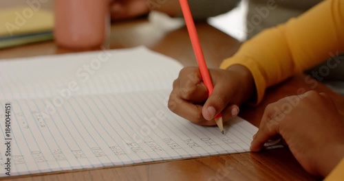 Pressing red pencil, hand is writing in lined notebook for practice on desk with pink cup