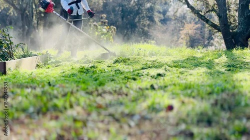 Man Operating a Brush Cutter to Trim Grass and Weeds on a Field in the Morning