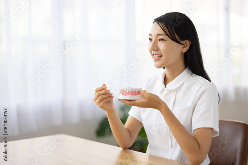Woman in white coat demonstrating tooth brushing with dental model