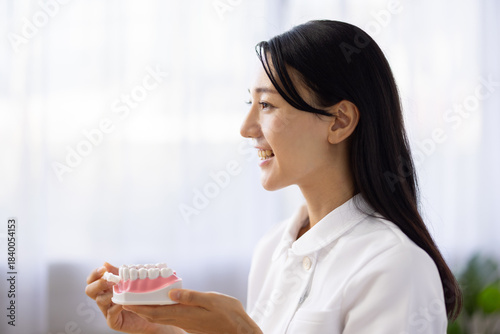 Woman in white coat demonstrating tooth brushing with dental model