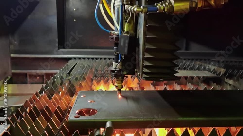 old industrial CNC laser cutting holes in sheet steel part with sparks in dark environment.