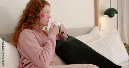 Diverse female friends in pjs sitting on bed sipping wine after pan, chatting with pink eye-patches