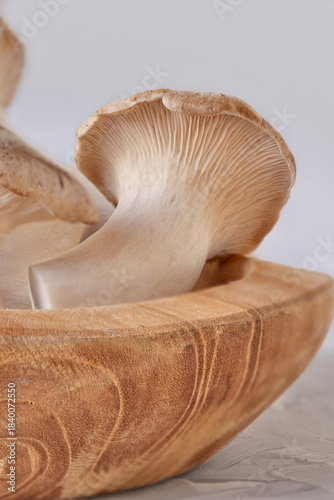 macro photo of a group of fresh king trumpet mushrooms lying in a wooden texture bowl on a white table