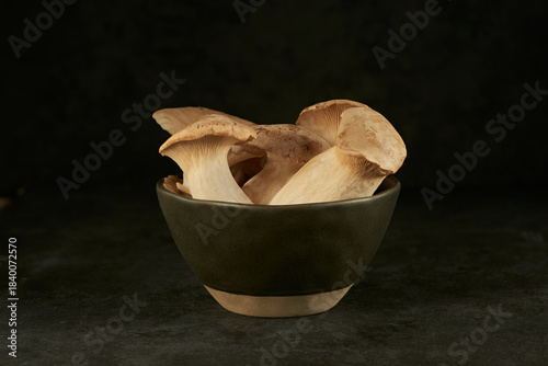 macro photo of a group of fresh king trumpet mushrooms lying  in a black ceramic bowl