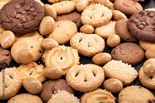 Close-up assortment of mixed cookies, including Danish butter cookies, sugar-topped cookies, swirl cookies, chocolate chip cookies, and caramel-coated nuts.