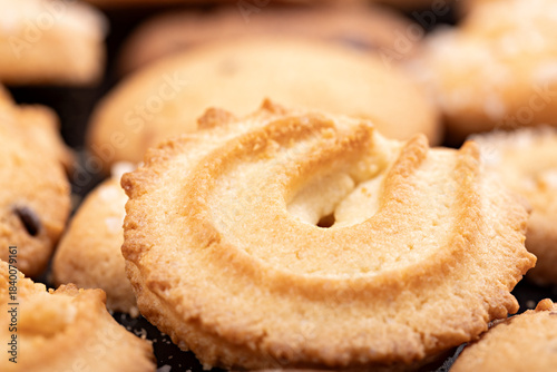 Close-up of a classic Danish butter cookie highlighting its golden color, crumbly texture, and decorative swirl shape. The shallow depth of field emphasizes the surface details and buttery crisp edges