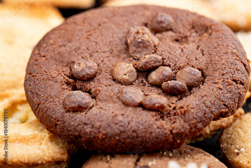 Close-up of a chocolate cookie topped with chocolate chips, showcasing its rich cocoa color, crumbly baked texture, and surface details.