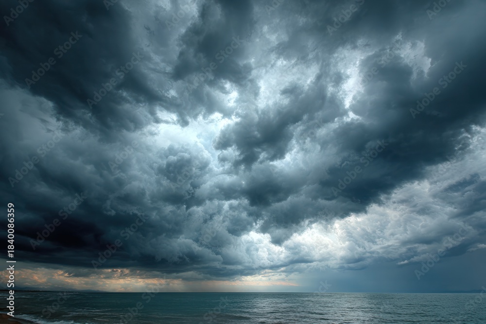 Obraz premium Celestial Canvas: A vast, dramatic canvas of turbulent clouds dominates the seascape, creating an atmosphere of impending weather. capturing the awe-inspiring beauty of nature's forces