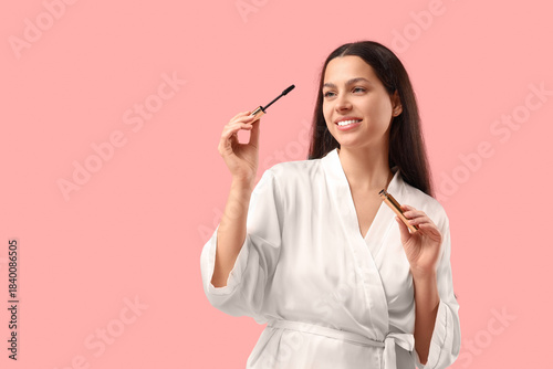Pretty young woman in bathrobe with mascara on pink background