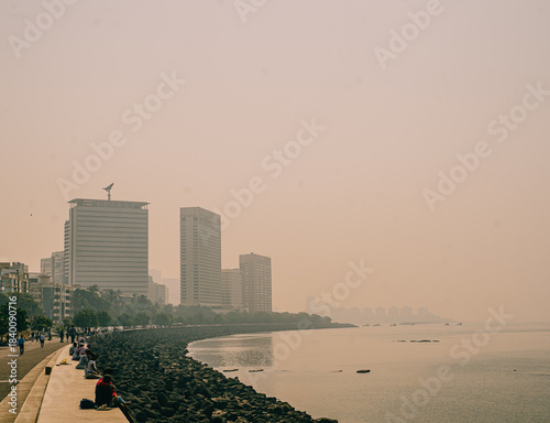 Mumbai, India Coastal urban view of Marine Drive in Mumbai with people sitting along the seawall and high-rise buildings fading into warm haze. A calm waterfront cityscape at the Arabian Sea.