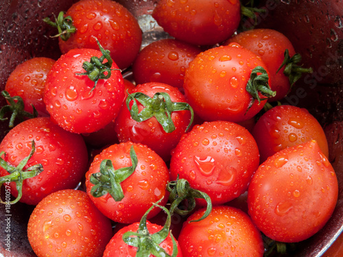 Foto Bunch of fresh red cherry tomatoes rinsed in the bowl with water in the sink, close up of tomatoes in the bowl covered with water drops