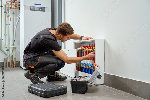 Technician inspecting underfloor heating manifold with pipes and valves in utility room. Concept of heating installation, plumbing maintenance, HVAC service and residential energy system
