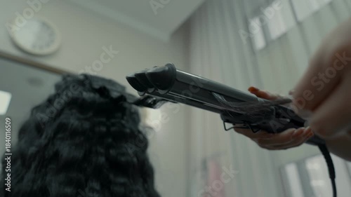 A special curling iron for hair is used to make wavy hair in a hairdressing salon. Beauty salon.