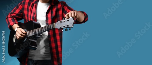 Obraz na plátně Young man with guitar on blue background with space for text, closeup