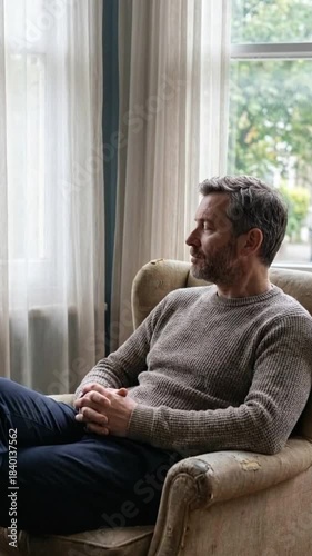 Thoughtful man sitting in an armchair by the window, reflecting in a cozy environment