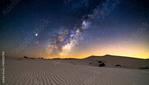 Milky Way arches above a desert landscape, stars illuminate patterned sand dunes under a vivid night sky