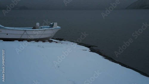 岸辺に陸揚げされた小さな漁船のある雪景色