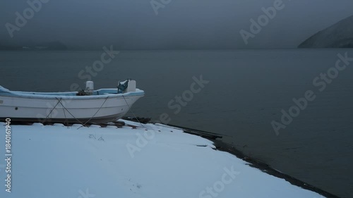 岸辺に陸揚げされた小さな漁船のある雪景色