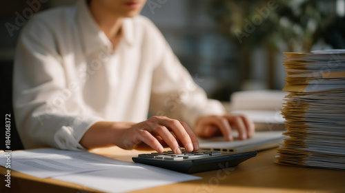An office worker verifying invoice details on a spreadsheet, cross-checking numbers with receipts stacked beside the keyboard — routine accounting verification and administrative workflow.