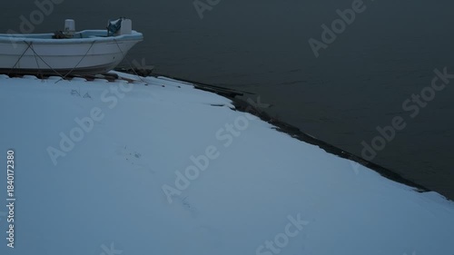 岸辺に陸揚げされた小さな漁船のある雪景色