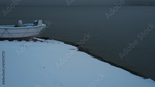 岸辺に陸揚げされた小さな漁船のある雪景色