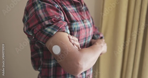 Asian senior woman looking on camera with diabetes patch on arm at home - Lifestyle and people diseases concept