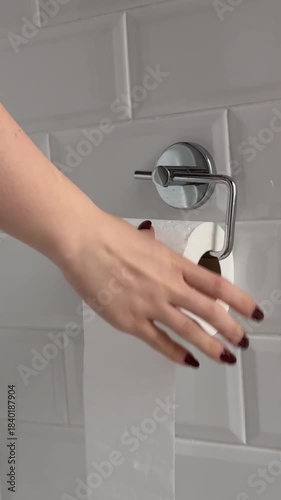 Hand tears off toilet paper in holder. Unwise consumption of toilet paper, too much paper needed when using toilet wc bathroom, washroom. Close Up male hand, steel paper holder gray bathroom wall.