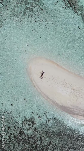 Drone topdown pullout shot of friends laying on a white sand bar enjoying the sun and clear blue waters of Fiji.