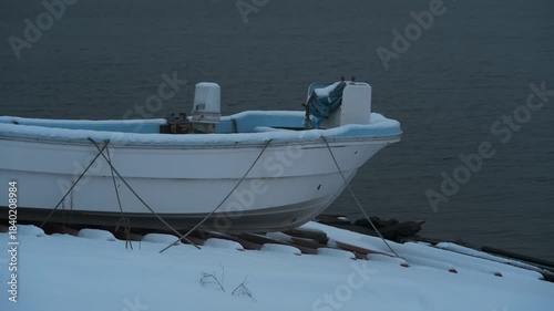 岸辺に陸揚げされた小さな漁船のある雪景色