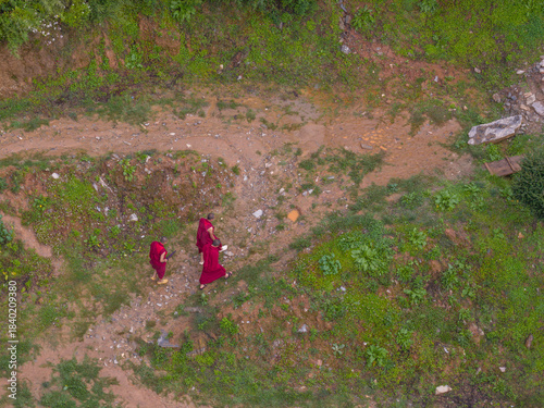 Aerial view of monks in deep red robes walking along a winding path, cutting through vibrant green slopes, the scene a blend of solemnity and natural beauty, Paro, Bhutan.