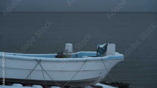 岸辺に陸揚げされた小さな漁船のある雪景色