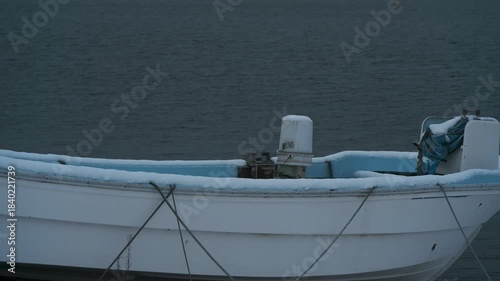 岸辺に陸揚げされた小さな漁船のある雪景色