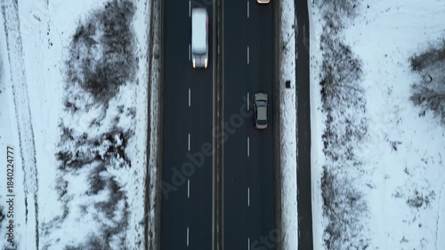 Aerial view of a cars driving along a snow-covered road, showcasing the vehicle's movement and the surrounding winter landscape, camera follows cars smoothly. Autos riding at highway at cold season