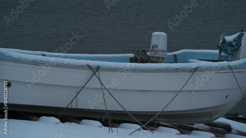 岸辺に陸揚げされた小さな漁船のある雪景色