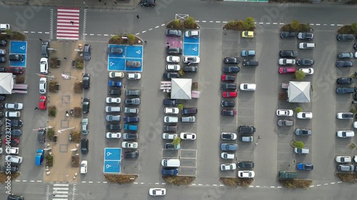 Aerial view of busy parking lot near shopping center, showcasing various vehicles in organized rows, with gradual camera zoom out revealing scene dynamics and spatial arrangement