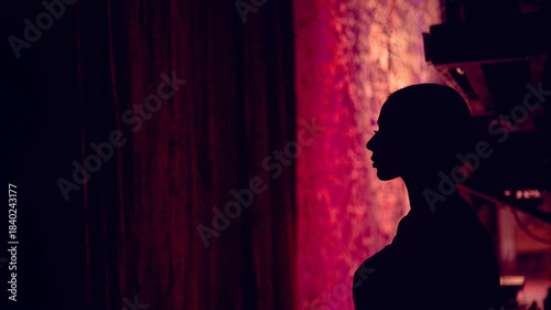 Foto Ballerina side silhouette positioned near stage curtains in low light