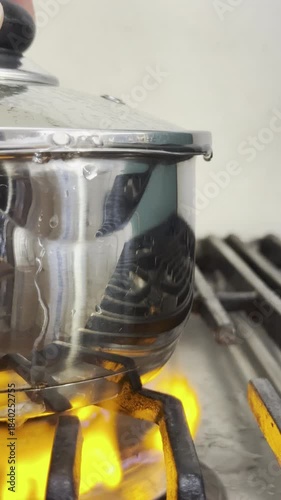 Vertical video social media - Closeup of a stainless steel pan on a gas cooker hob, with boiling water spilling out beneath the lid and over the sides, and turning the blue flame to orange.