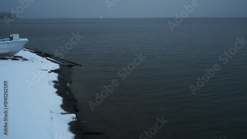 岸辺に陸揚げされた小さな漁船のある雪景色