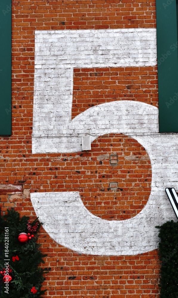 Fototapeta premium The number 5 painted on the brick wall of a building 