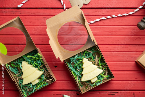 Homemade lotion bars in tree shapes in gift boxes on a red wooden background.